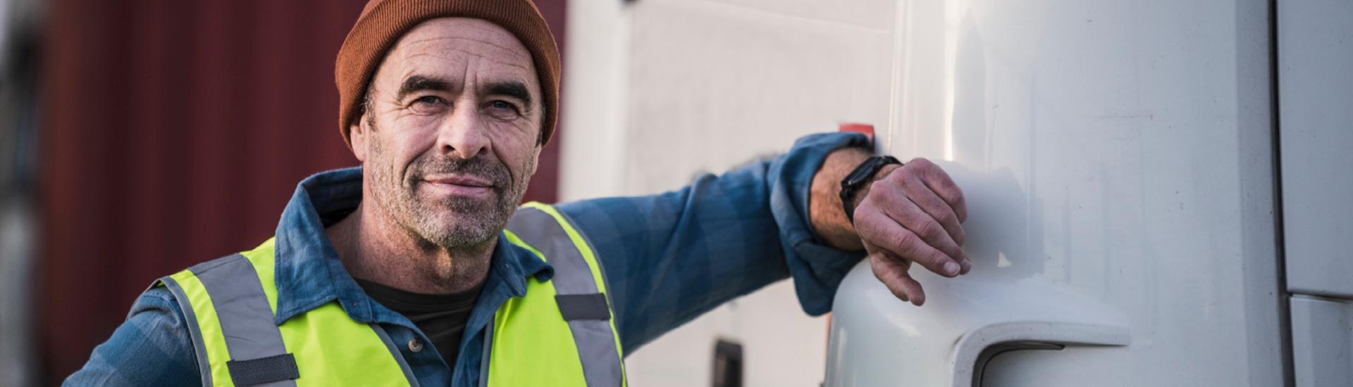 Älterer Lkw-Fahrer mit Rettungsweste lehnt an LKW