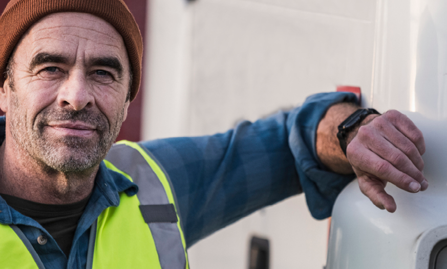 Älterer Lkw-Fahrer mit Rettungsweste lehnt an LKW