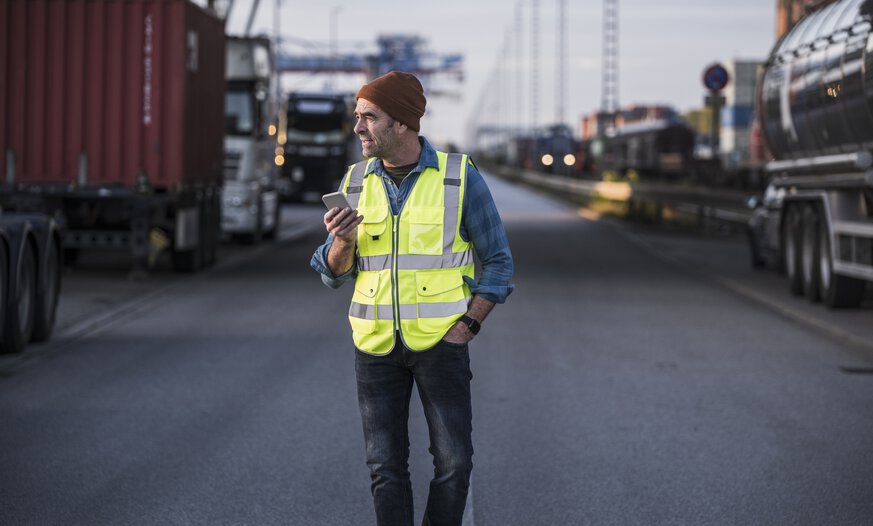 Mann mit Warnweste und Handy läuft zwischen Containern