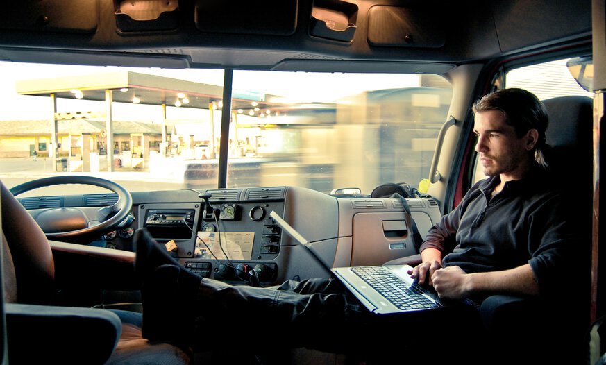Lkw-Fahrer sitzt in Fahrerkabine mit Laptop