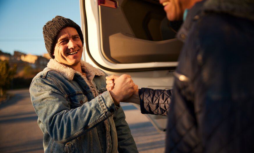 Mann mit Mütze begrüßt Lkw-Kollegen auf Parkplatz