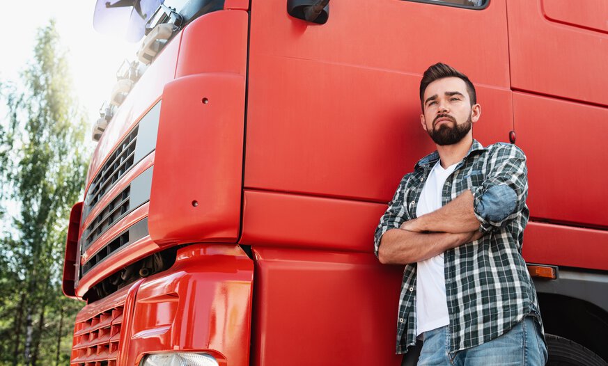 Junger Mann in kariertem lockeren Hemd steht angelehnt vor rotem Lkw