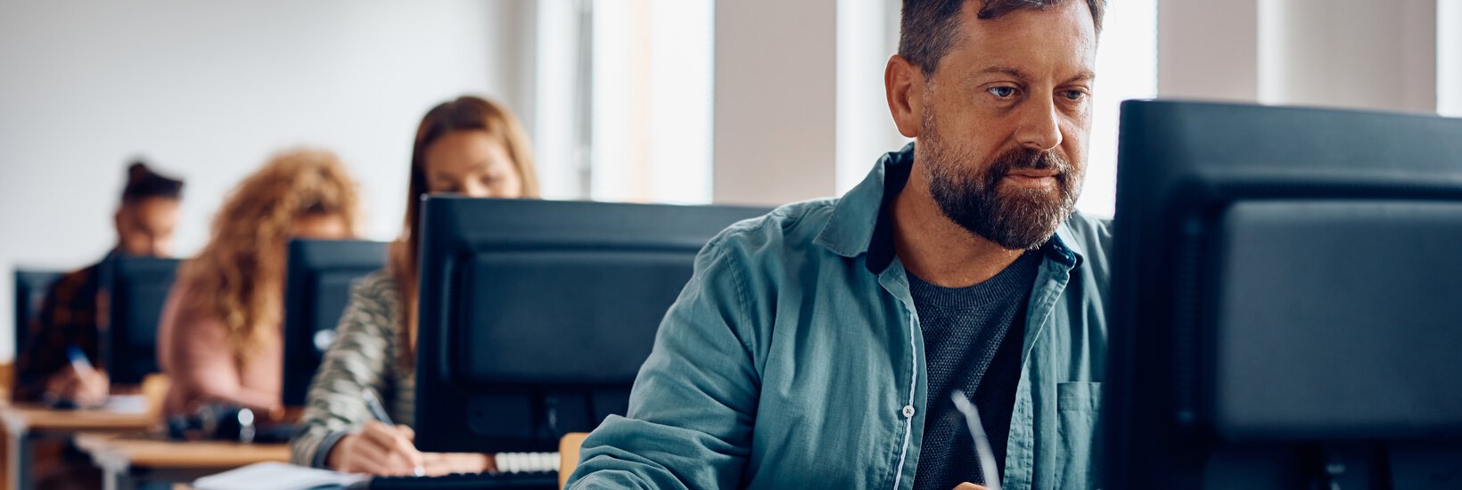 Mann am Computer Mann mittleren Alters im blauen Jeanshemd sitz hinter Computer und lernt