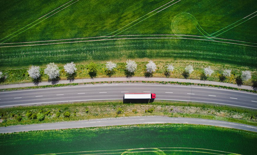 Luftaufnahme eines roten Lkws auf Landstraße zwischen gründen Feldern