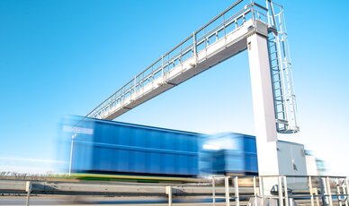 Blauer Lkw fährt auf Autobahn durch eine Zollbrücke