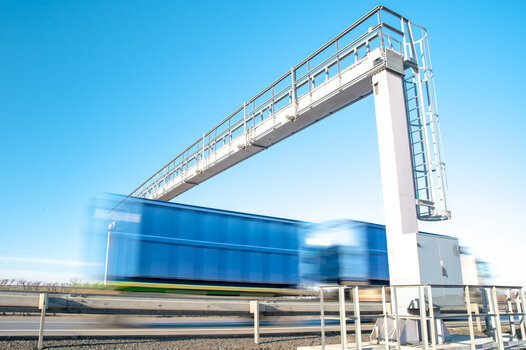 Blauer Lkw fährt auf Autobahn durch eine Zollbrücke