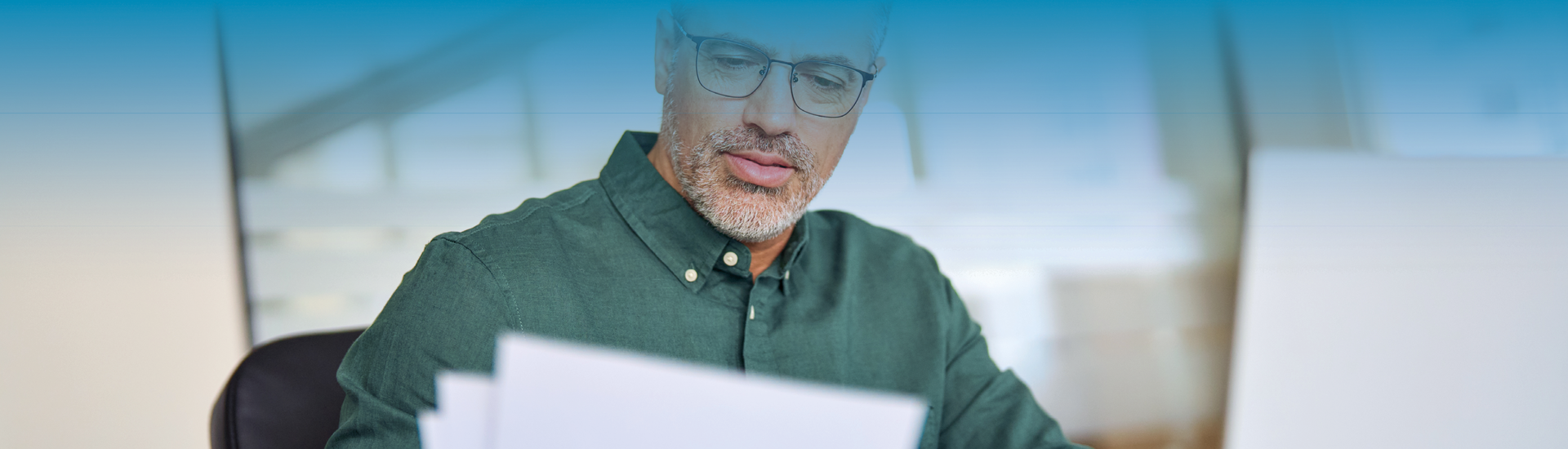 Mann mit grünem Hemd schaut sich Papiere am Schreibtisch an